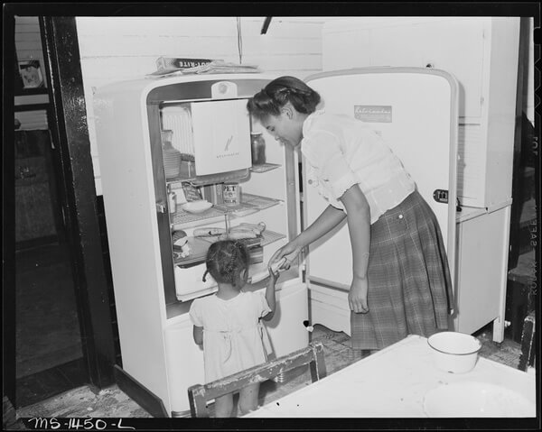 Mrs. Howard giving her daughter a snack from the refrigerator (West Virginia, U.S. Dept of the Interior, 1946).