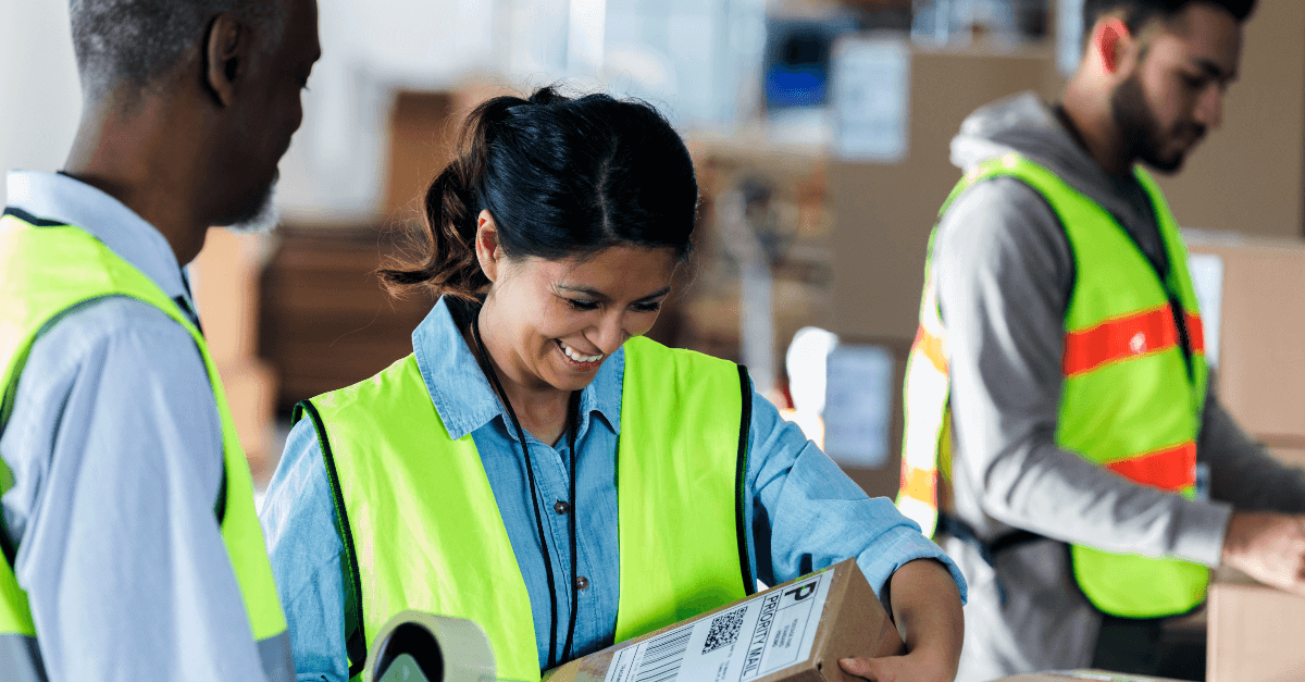A woman warehouse worker wearing a neon vest at work smiling