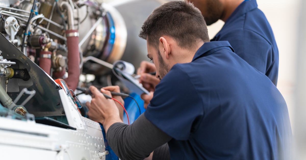 Technicians performing aerospace quality assurance by testing and inspecting aircraft engine components with diagnostic tools on a maintenance line.