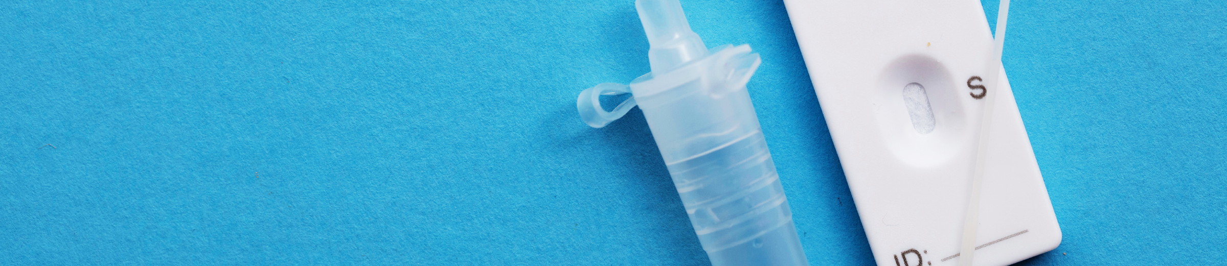 A white rapid antigen test kit with a testing device, dropper bottle, and swab placed on a blue background. The testing device shows a negative result with only one line visible under the ‘C’ window. A dropper bottle containing a clear solution and a white swab are also present.
