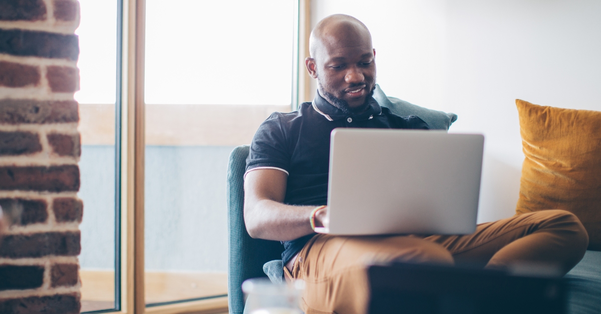 Man sitting casually on a couch in a cozy home setting, working on a laptop and using artificial intelligence  to update his resume. 