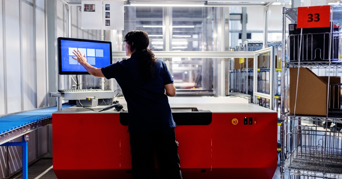 A young woman in a distribution warehouse is updating package details on a computer. She is focused on the screen, with shelves of packages and boxes in the background, indicating a busy and organized workspace. She is an example of how automation is changing warehouse work. 