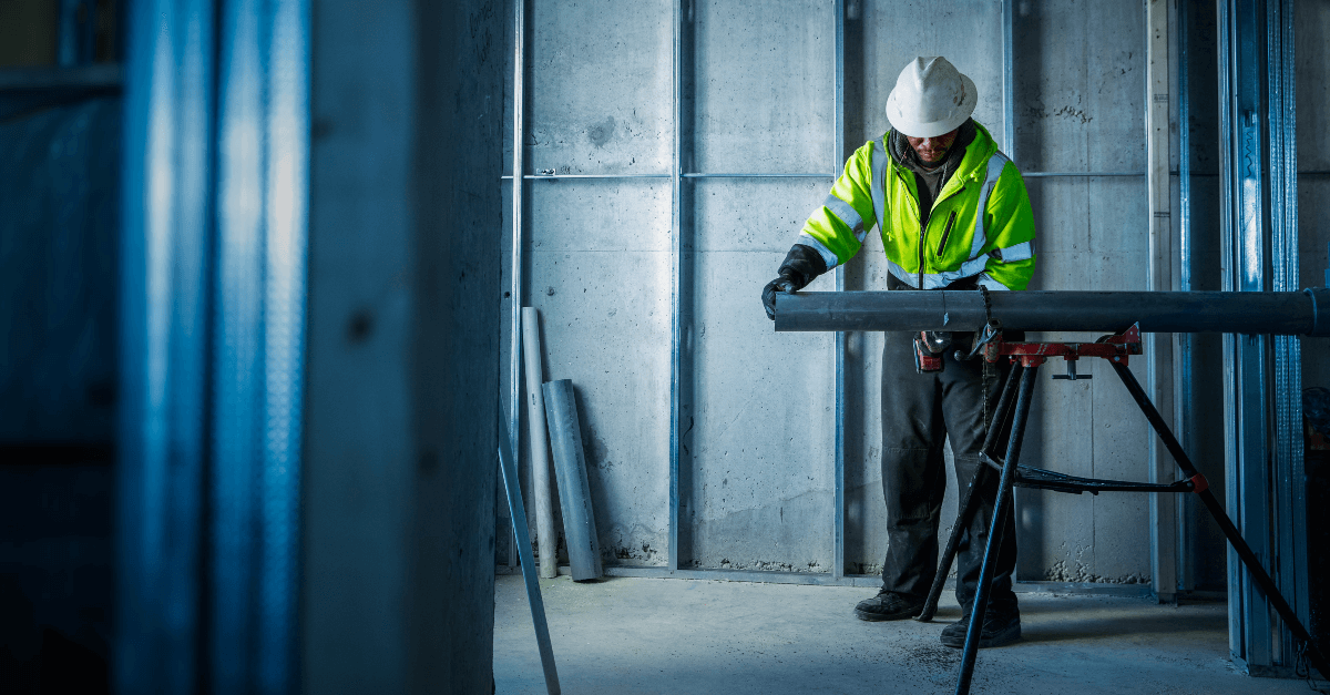 A worker in a yellow reflective vest works on a table saw.