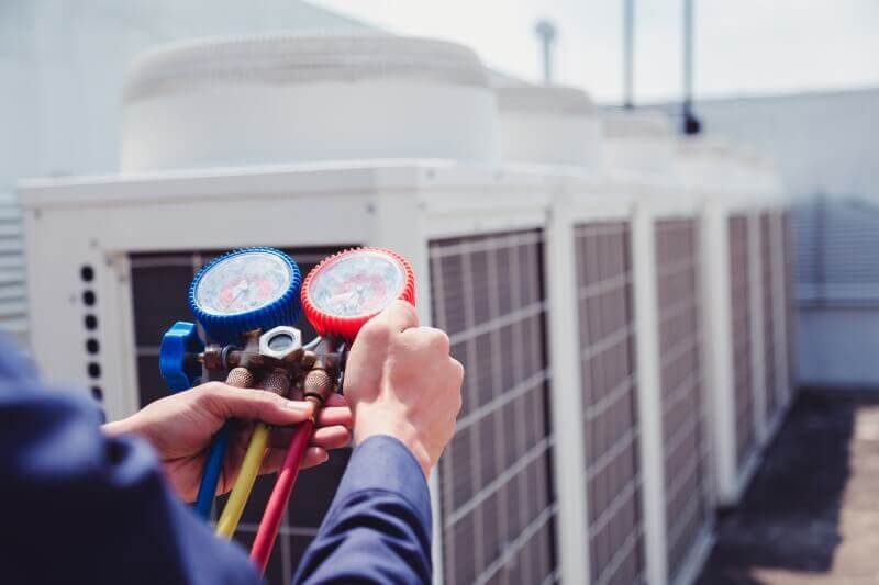 The photo focuses on the hands of a facilities mechanic checking a rooftop air conditioner.