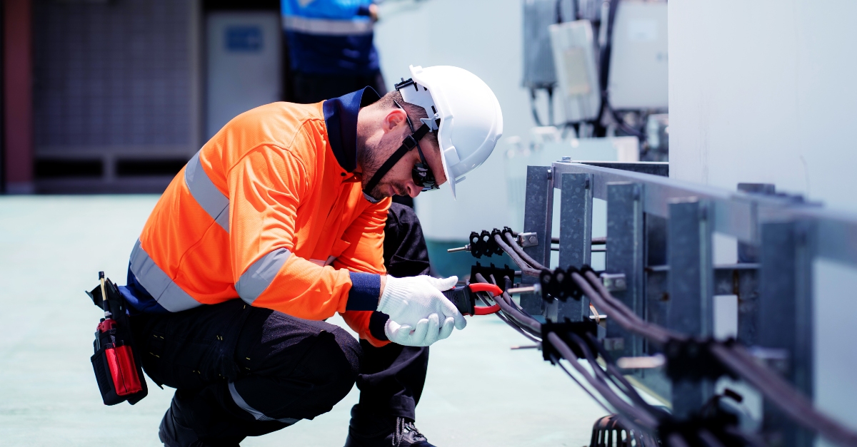 Industrial electrician working on rooftop electrical system maintenance at a commercial facility.