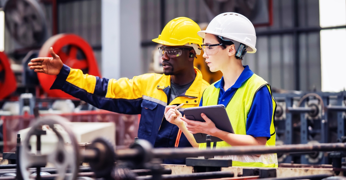Industrial maintenance career concept: two industrial workers inspect machinery and discuss workflow on a production line, highlighting teamwork, troubleshooting and hands-on equipment maintenance in a manufacturing environment.