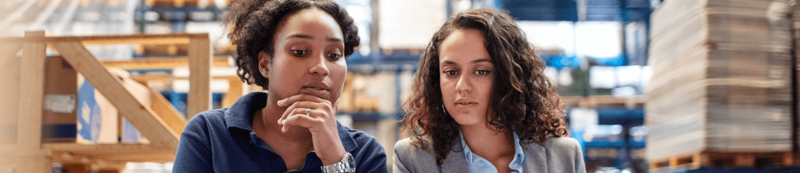 Two female workers stare off screen in a logistics environment