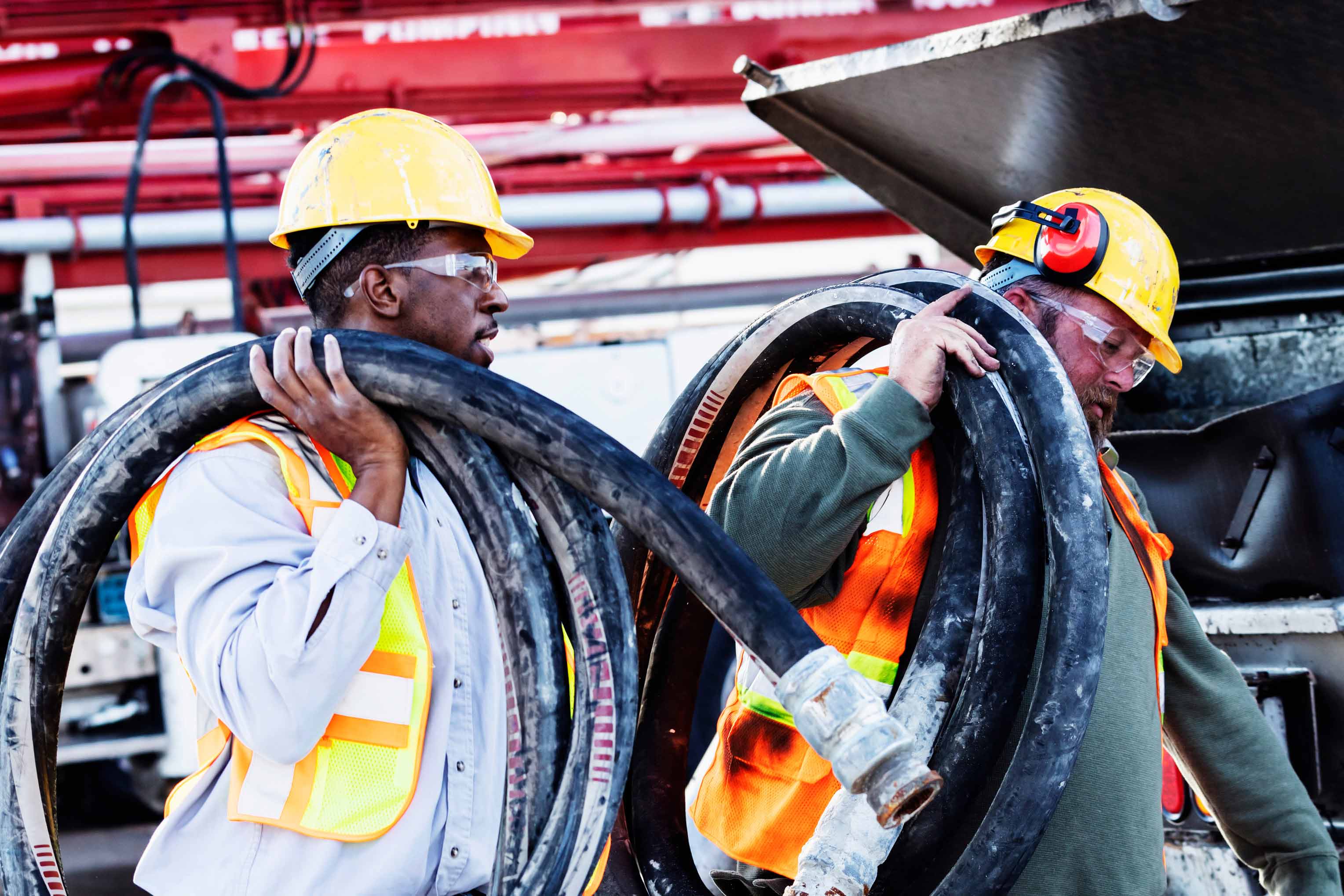 Construction workers wearing safety gear move large electrical conduit at an active job site, supporting power infrastructure installation for a data center construction project.