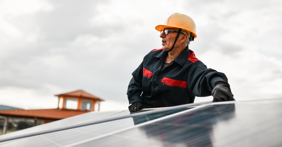 A solar construction worker wearing a hardhat, safety glasses, gloves and a heavy jacket places a solar panel onto an array