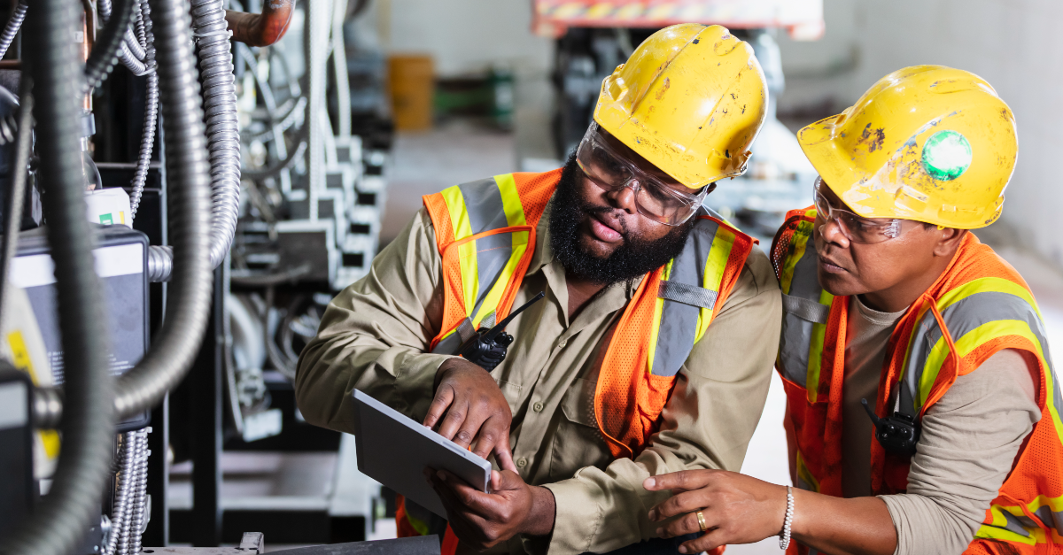 Two workers in protective gear inspecting industrial refrigeration equipment in a factory.