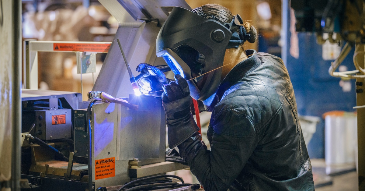 A welder focuses on repairing equipment in a factory setting. It demonstrates how welding technology is making work safer.