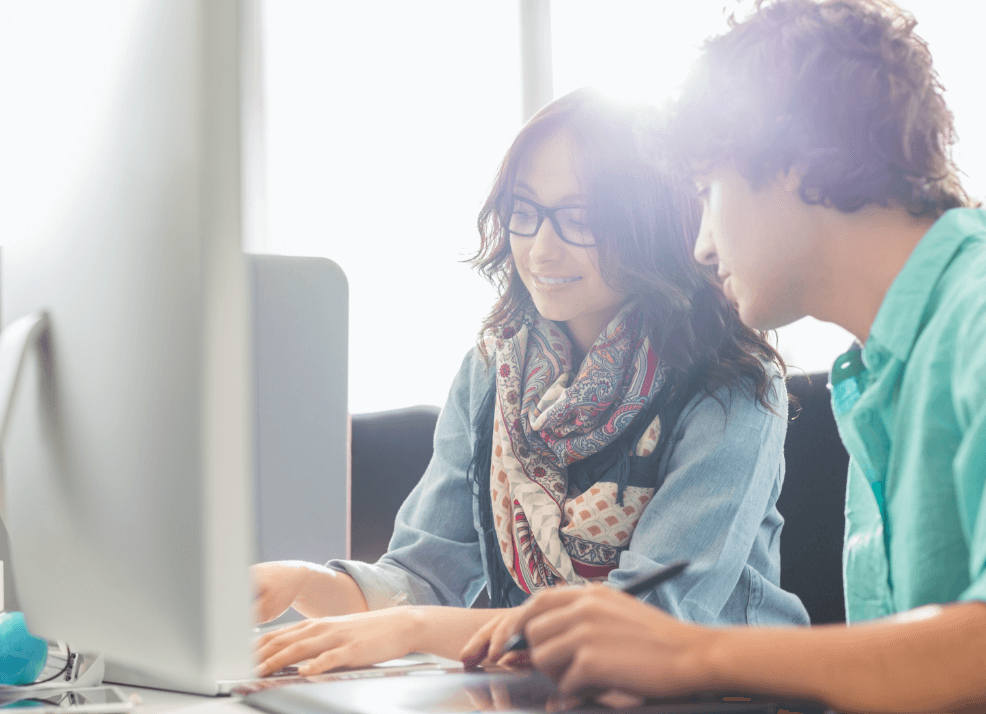 photo of young professionals working together at a computer monitor