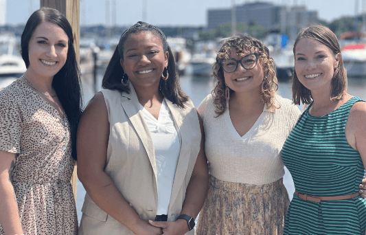 Four Aston Carter women employees posing in front of boats at an event.
