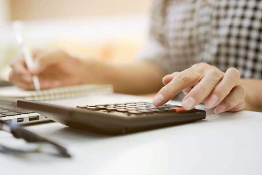 Talent acquisitions manager writing on legal pad to calculate cost effectiveness of new staffing plan 