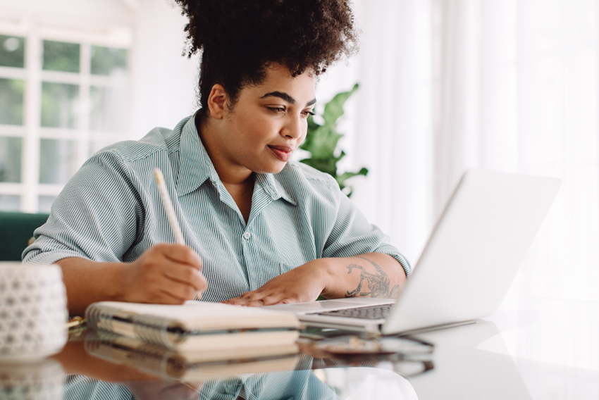 Woman works on her computer and a notepad