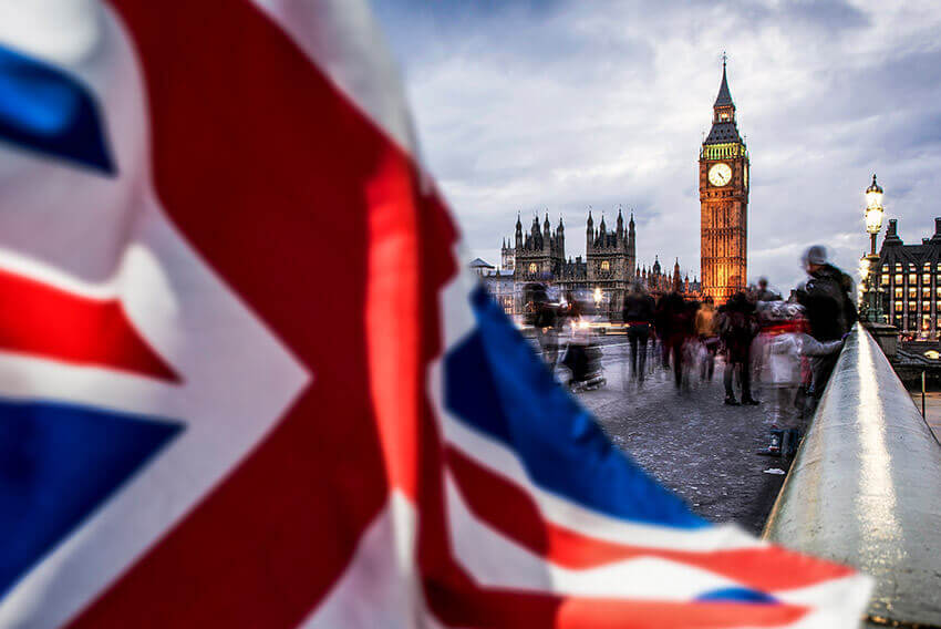 Up-close focus of Union Jack, UK national flag with clock appearing in the distance.