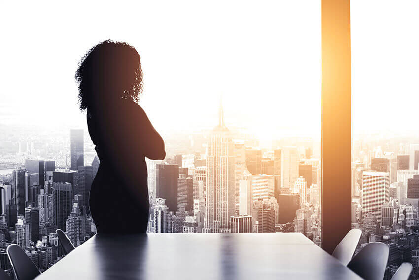 Une femme regardant par une fenêtre l’horizon d’une ville. Articles sur le recrutement d’Aston Carter