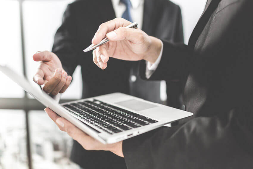 Two businessmen viewing managed services on a laptop. Aston Carter Staffing Articles.