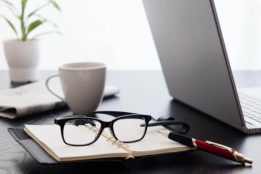 Glasses on an open planner with a pen on top of the open planner. 