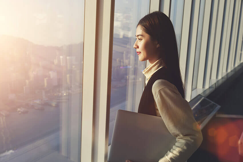 Une femme debout, tenant un ordinateur portatif et regardant l’horizon d’une ville. Articles sur le recrutement d’Aston Carter