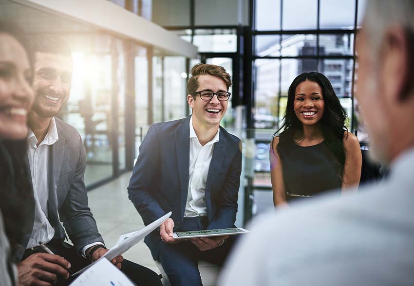 Male and female employees sitting in a group smiling and laughing in a meeting.