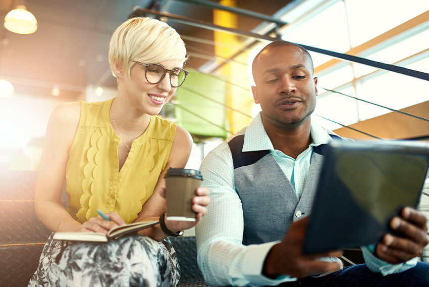 woman holding coffee looking at a tablet being held by a male coworker
