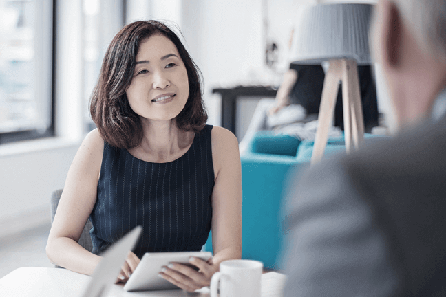 Professional woman holding a small notepad, sitting across and talking with another professional