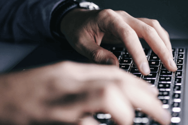 Male hands typing on a laptop keyboard. 